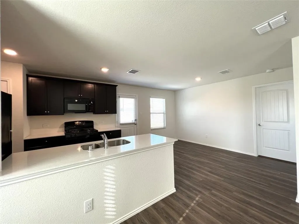 Open-concept living area featuring wood-finish flooring, recessed lighting, and a kitchen with dark cabinetry and a light-toned countertop