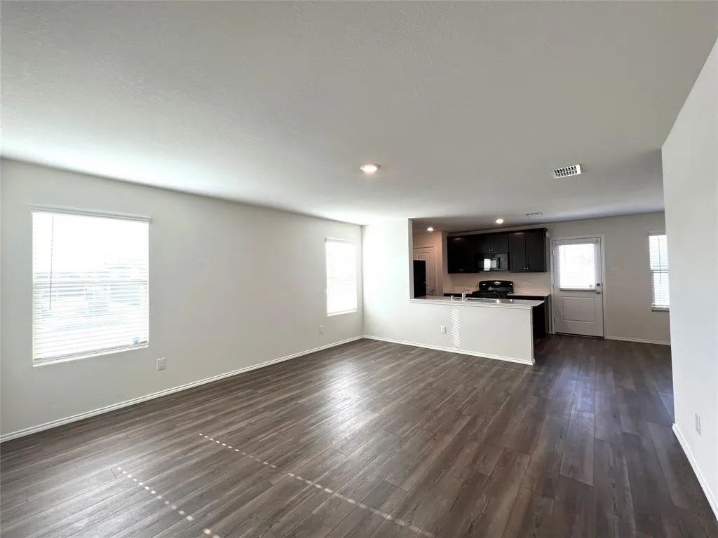 Open-concept living and kitchen area showcasing wood-finish flooring, recessed ceiling lighting, and abundant natural light from multiple windows