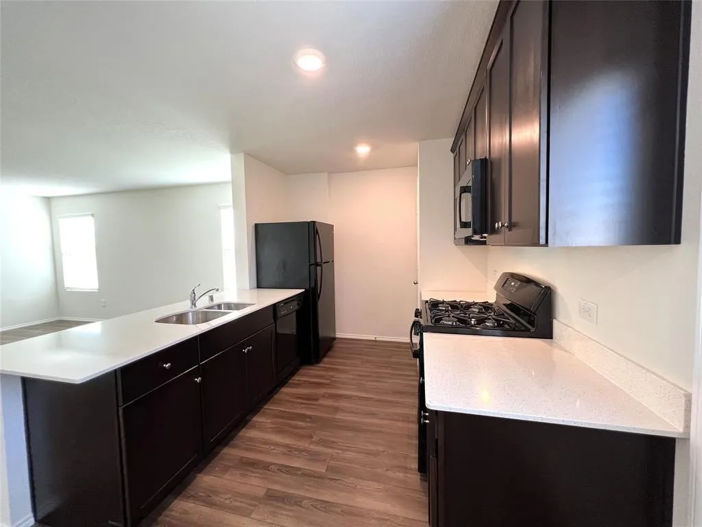 Kitchen featuring dark wood-finish cabinetry, white countertops, stainless steel sink, and wood-finish flooring