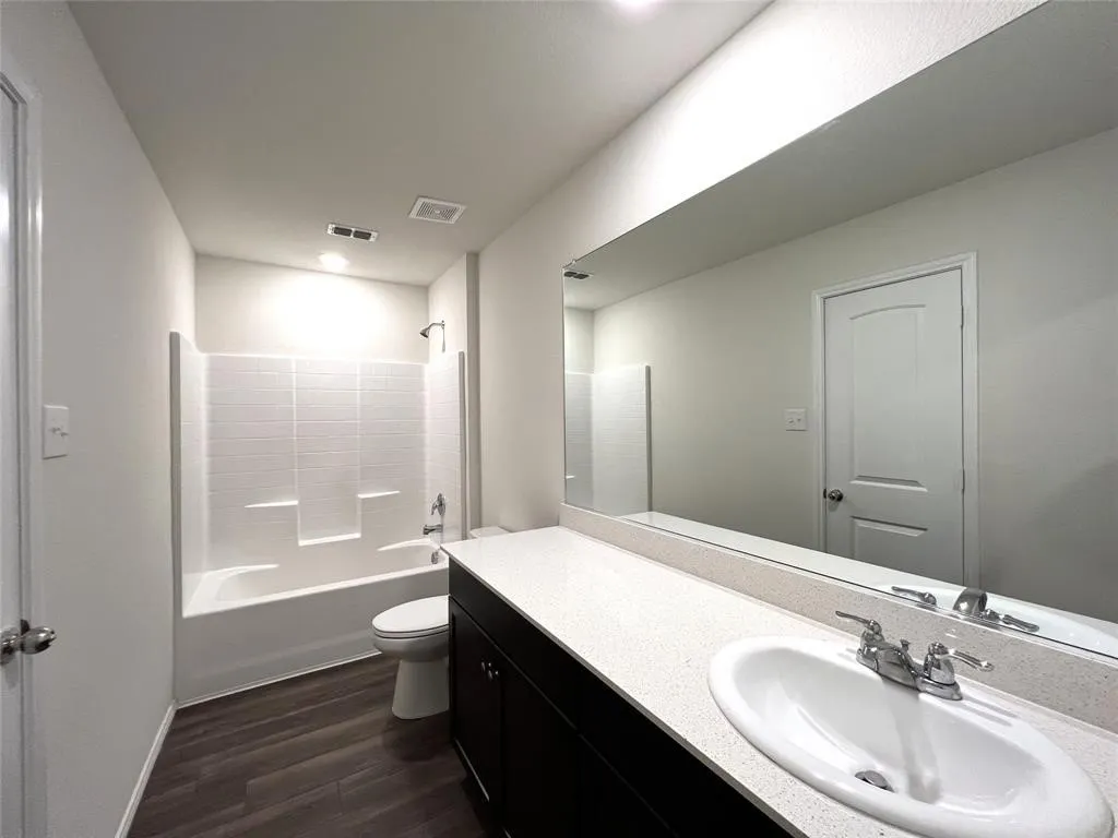 Spacious bathroom featuring a single vanity with a white countertop, an undermount sink, a large mirror, and a white tub with a shower