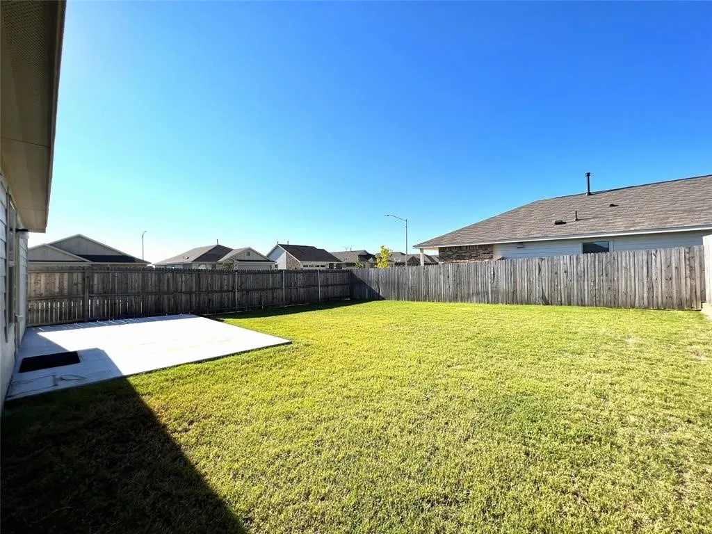 Expansive backyard featuring a manicured lawn, a large concrete patio, and a wood privacy fence