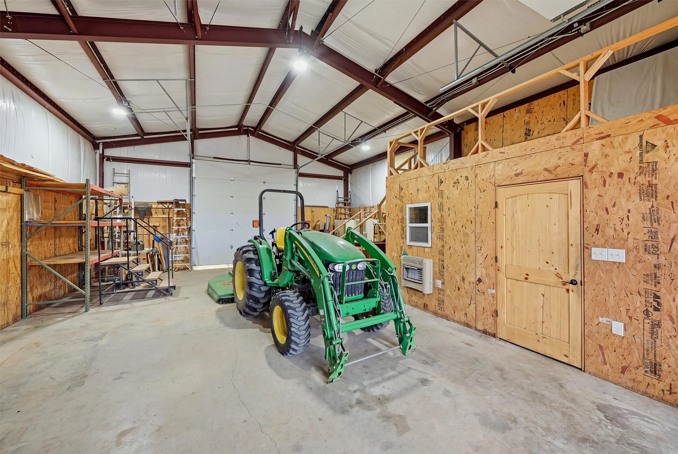 1200 square foot workshop interior featuring a concrete floor, high ceilings with exposed metal beams, and a large roll-up door