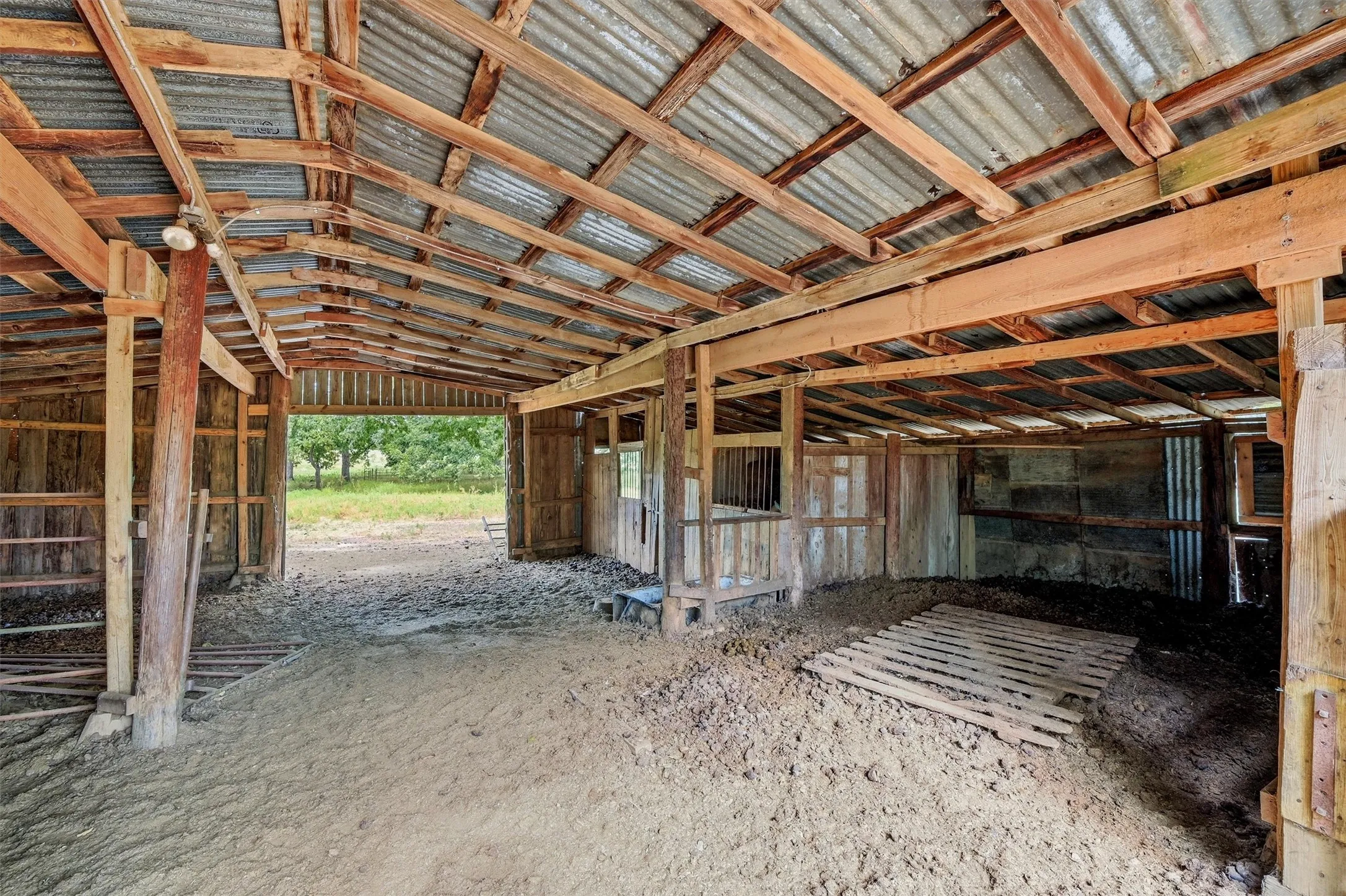 Open-air barn structure featuring exposed wood framing, corrugated metal roofing, and multiple stalls