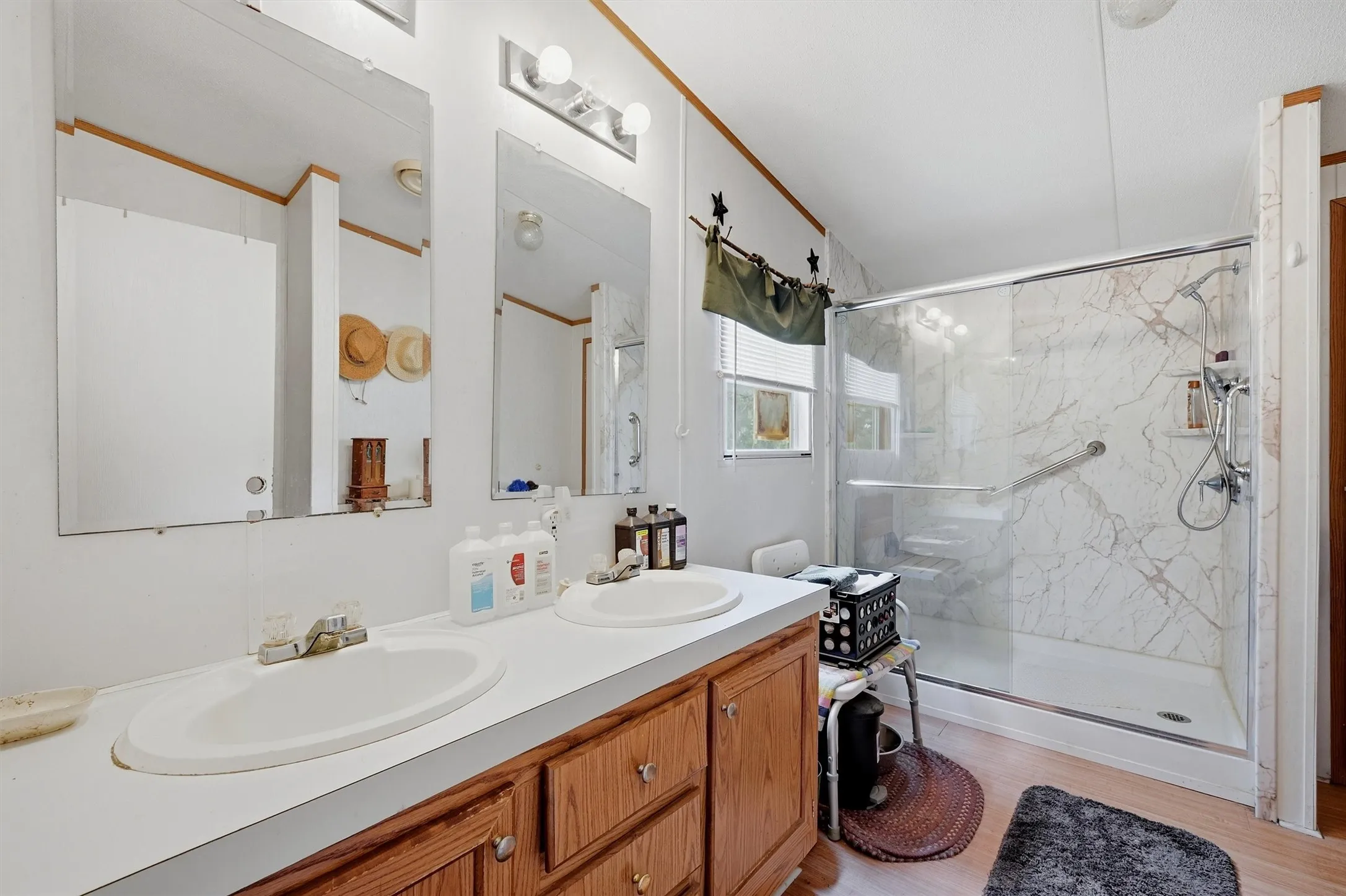 AI enhanced - primary bathroom with dual basin vanity with wood cabinetry, large mirrors, built-in lighting, and a glass-enclosed walk-in shower featuring a patterned surround