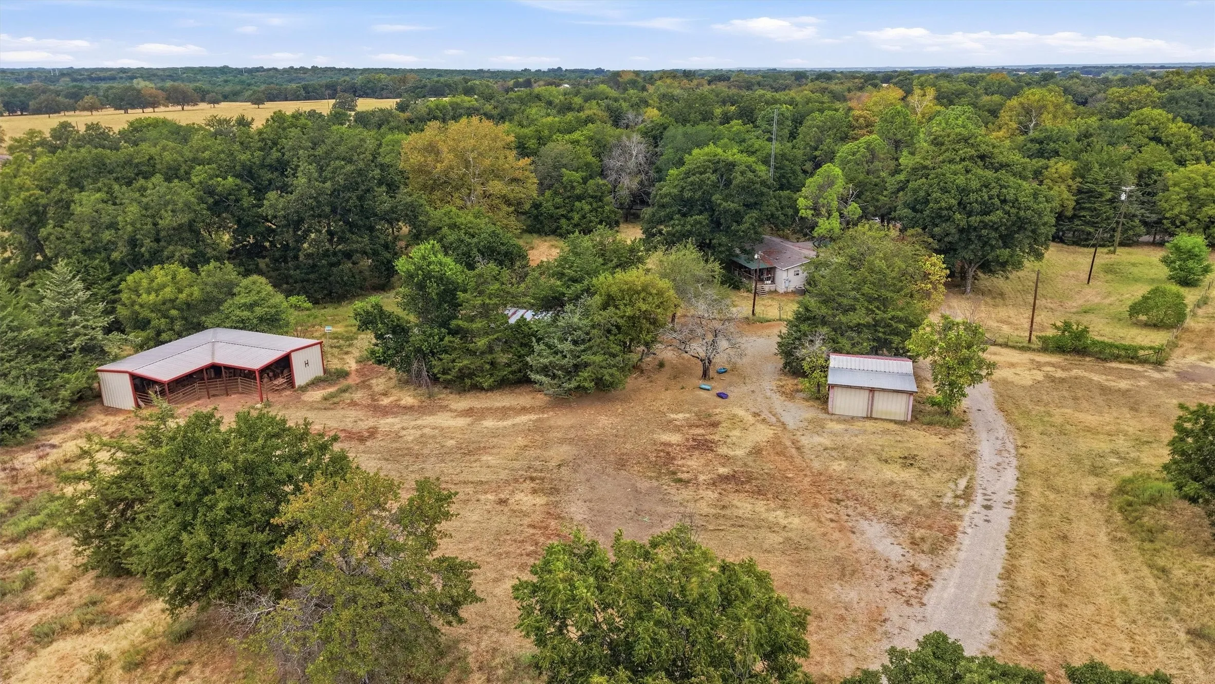Expansive acreage with mature trees, a detached structure with an open-sided shed, a second detached structure, and a main dwelling