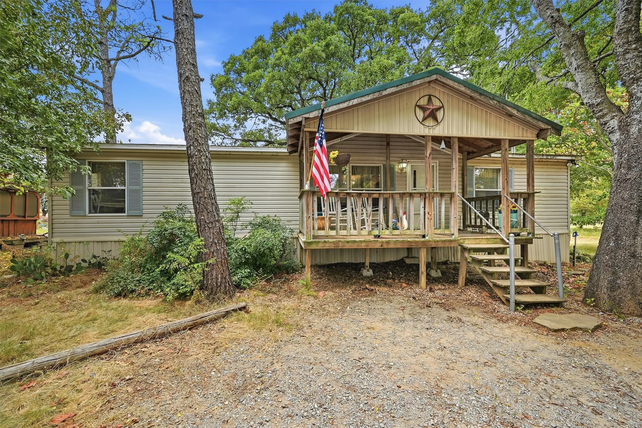 Covered front porch with wood railing and steps, vinyl siding exterior, and a gravel driveway