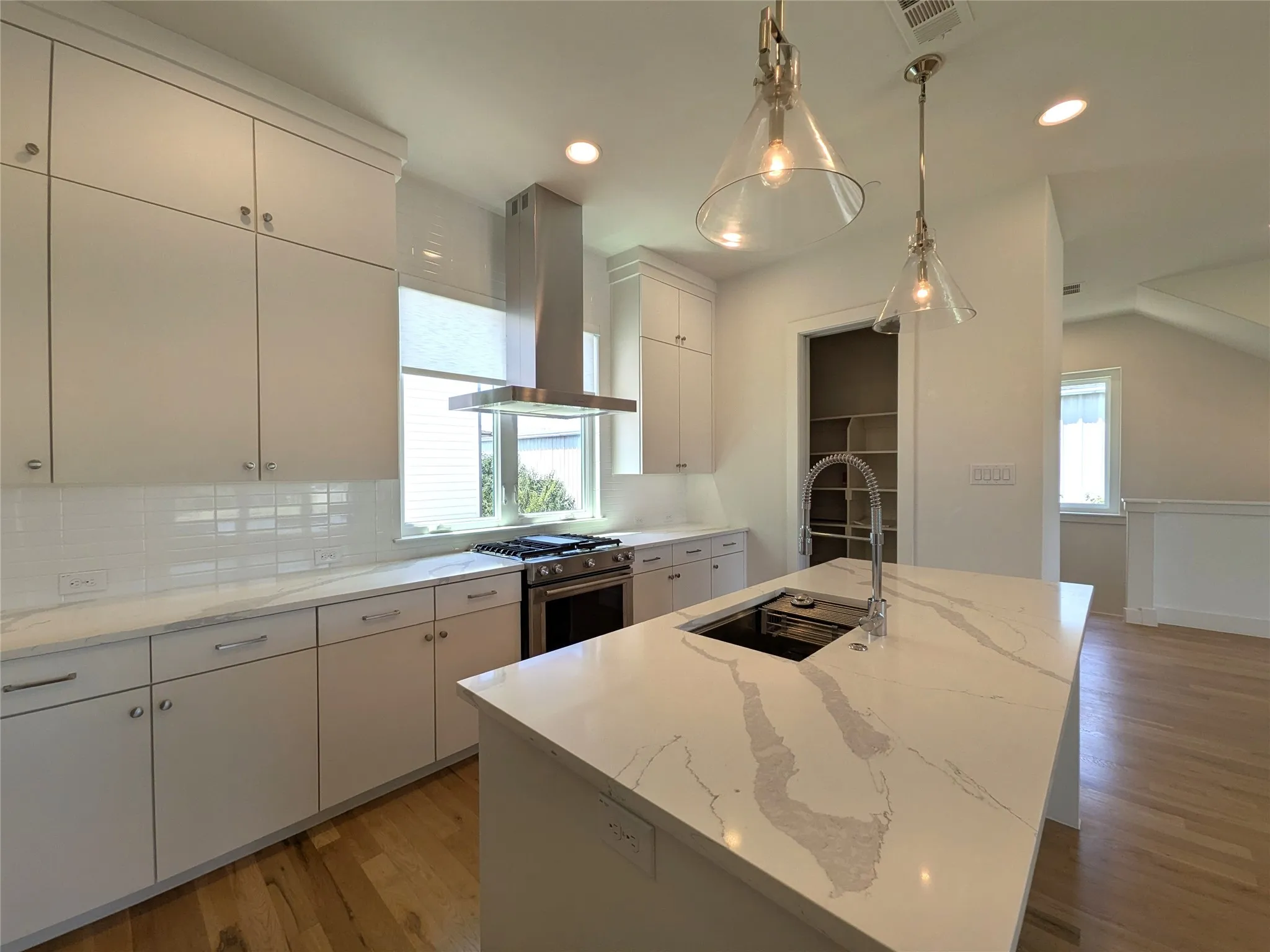 Kitchen featuring a central island with an undermount sink, white cabinetry, a stainless steel range, and a tile backsplash