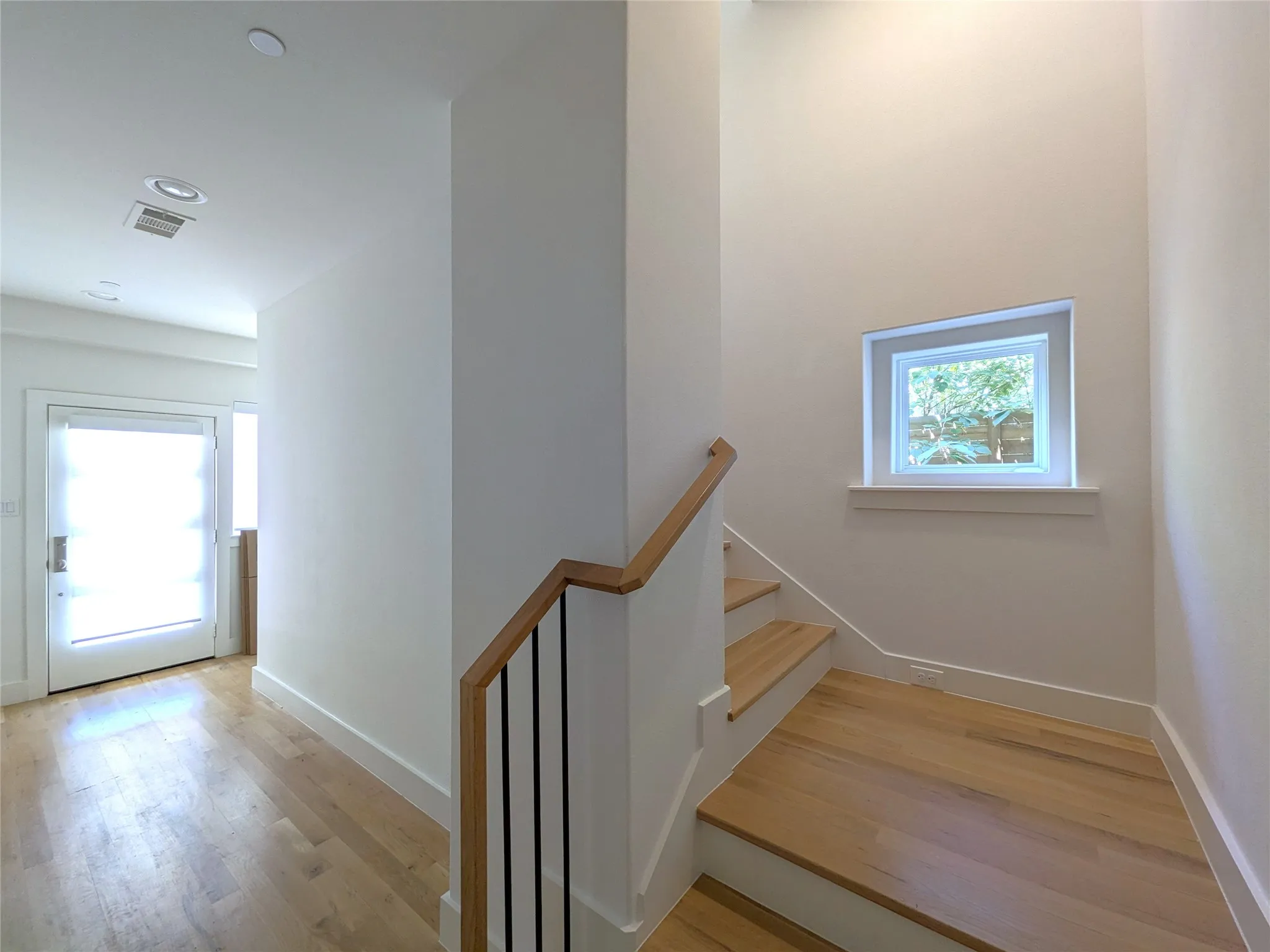 Hardwood flooring, recessed lighting, wood handrailing, and a window with white trim
