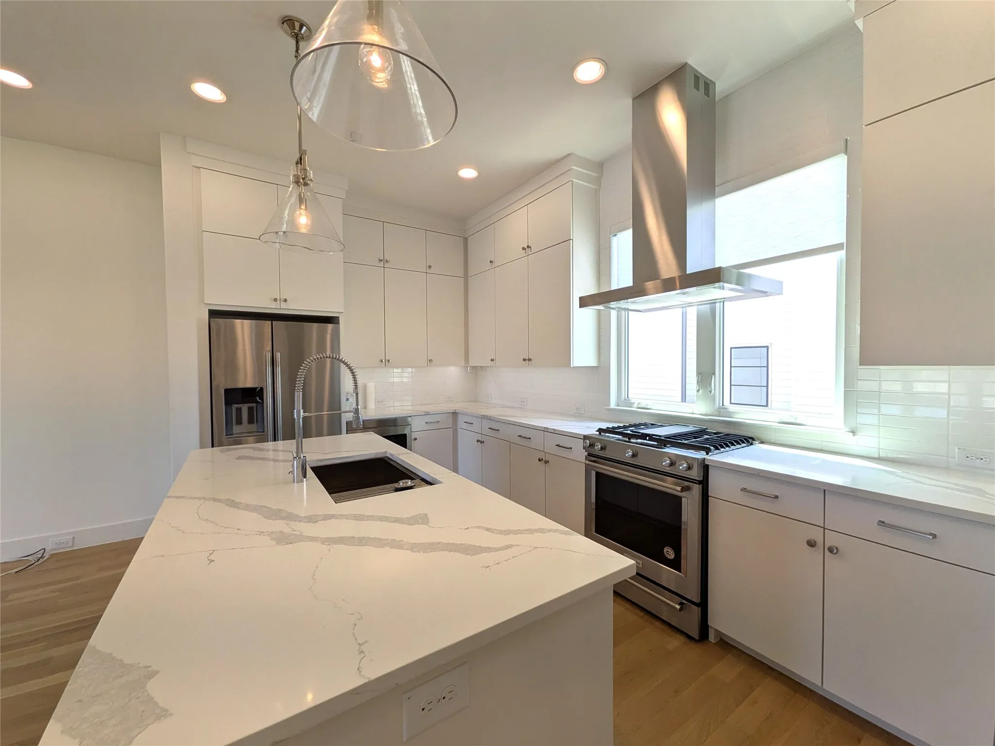Kitchen featuring an island with an undermount sink, stainless steel appliances, upper and lower cabinetry, clear glass pendant lighting, and recessed ceiling lights