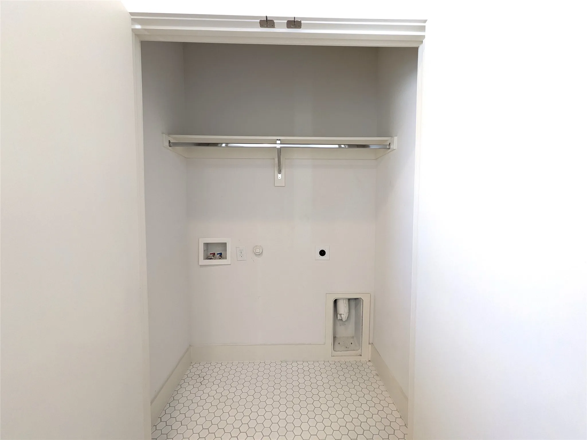 Recessed laundry area with hexagonal floor tiling and a chrome hanging rod