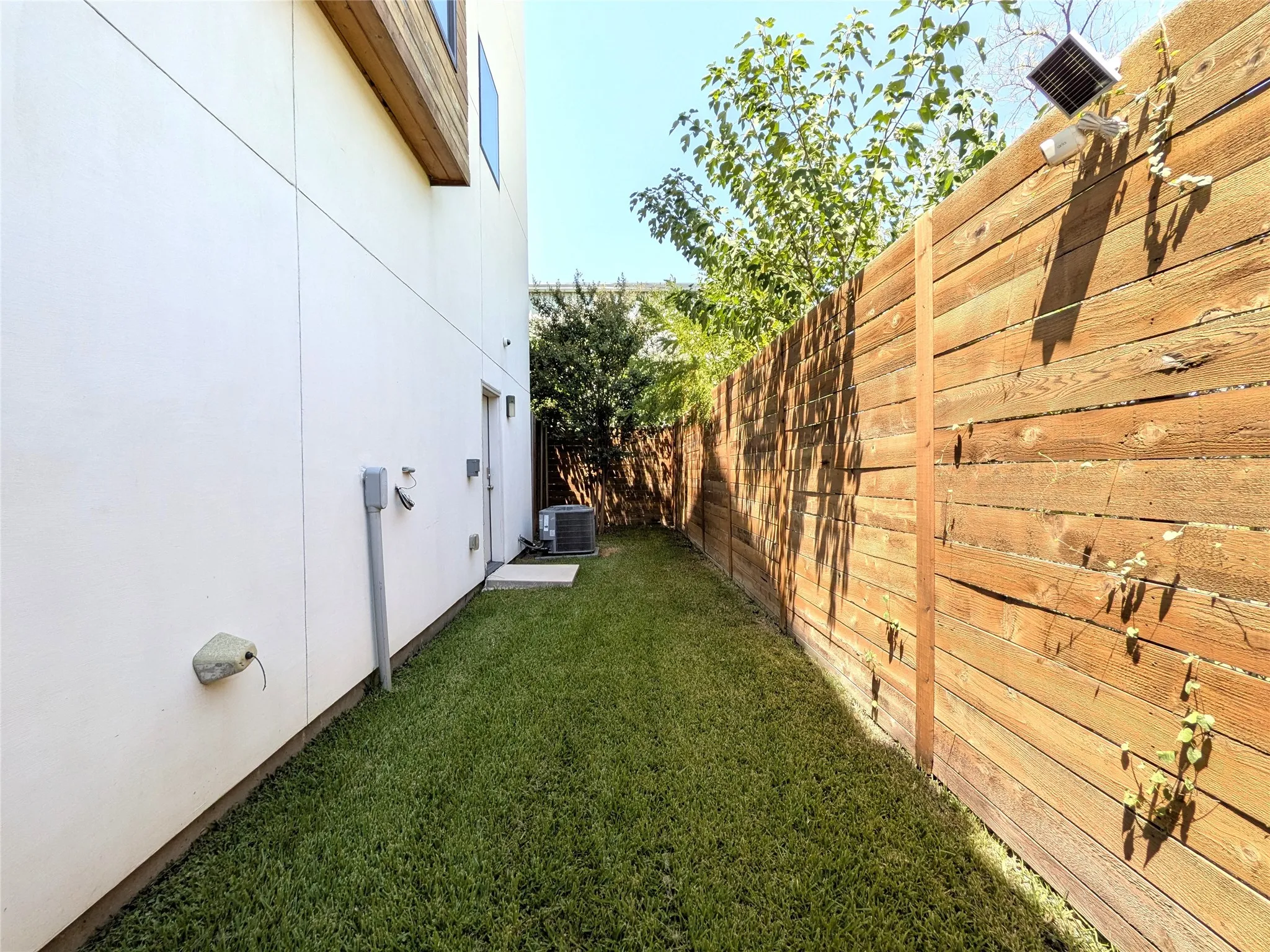 Grassed side yard featuring a wood fence, concrete pathway, and exterior wall with wood-finish trim