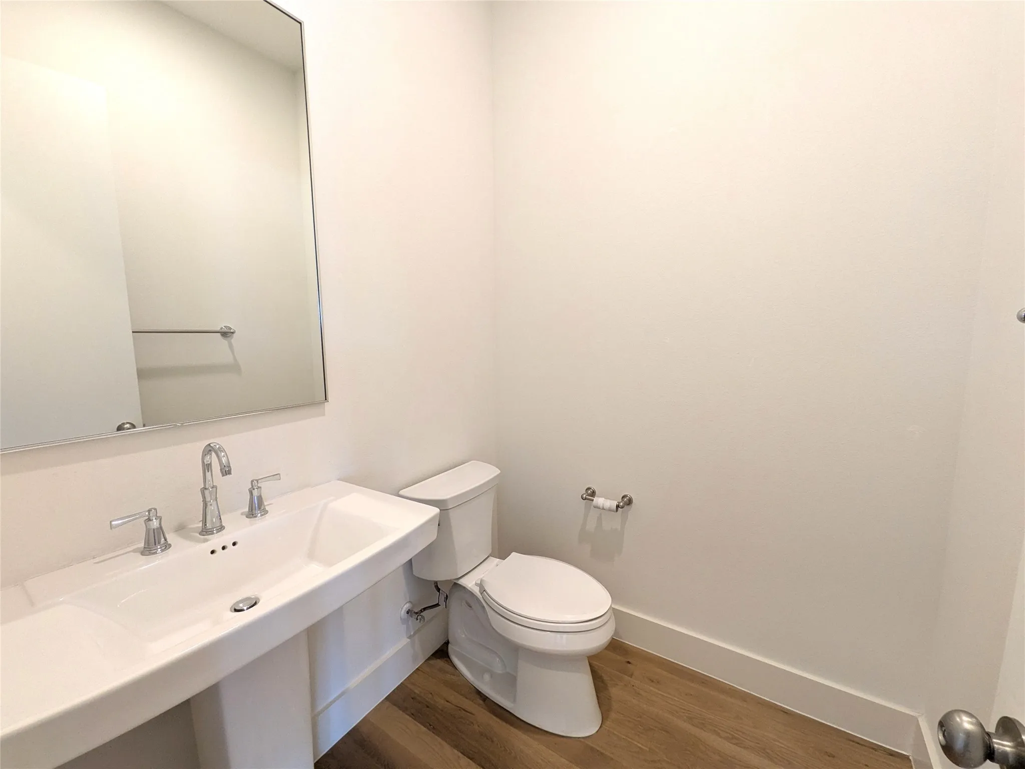 Contemporary powder room featuring a rectangular vessel sink with polished chrome faucet and widespread handles, white quartz countertop, large framed mirror, porcelain toilet with elongated bowl, and warm wood-finish flooring