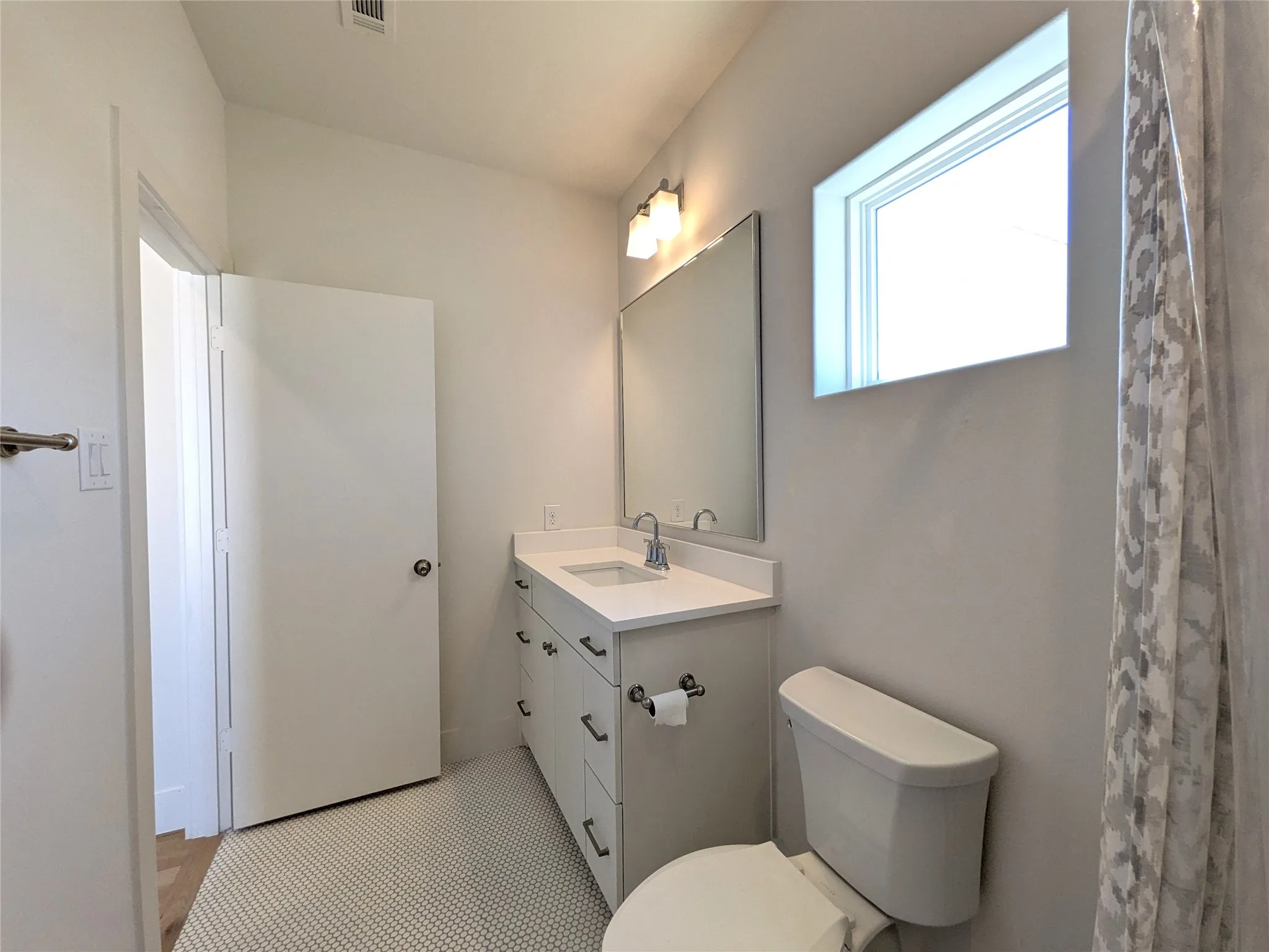 Vanity with a white countertop and integrated sink, chrome faucet, wall-mounted mirror, and a horizontal window
