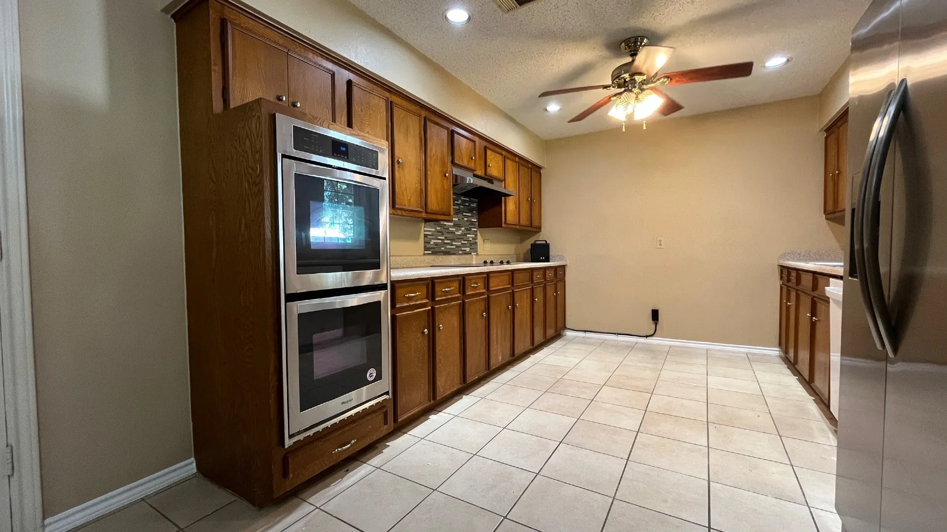 Stainless steel double wall oven, wood cabinetry, tile flooring, stainless steel refrigerator, and recessed lighting