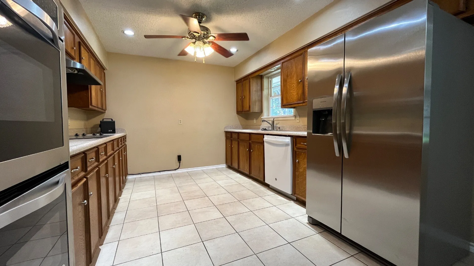Kitchen featuring tile flooring, wood cabinetry, stainless steel oven, stainless steel refrigerator, and a ceiling fan
