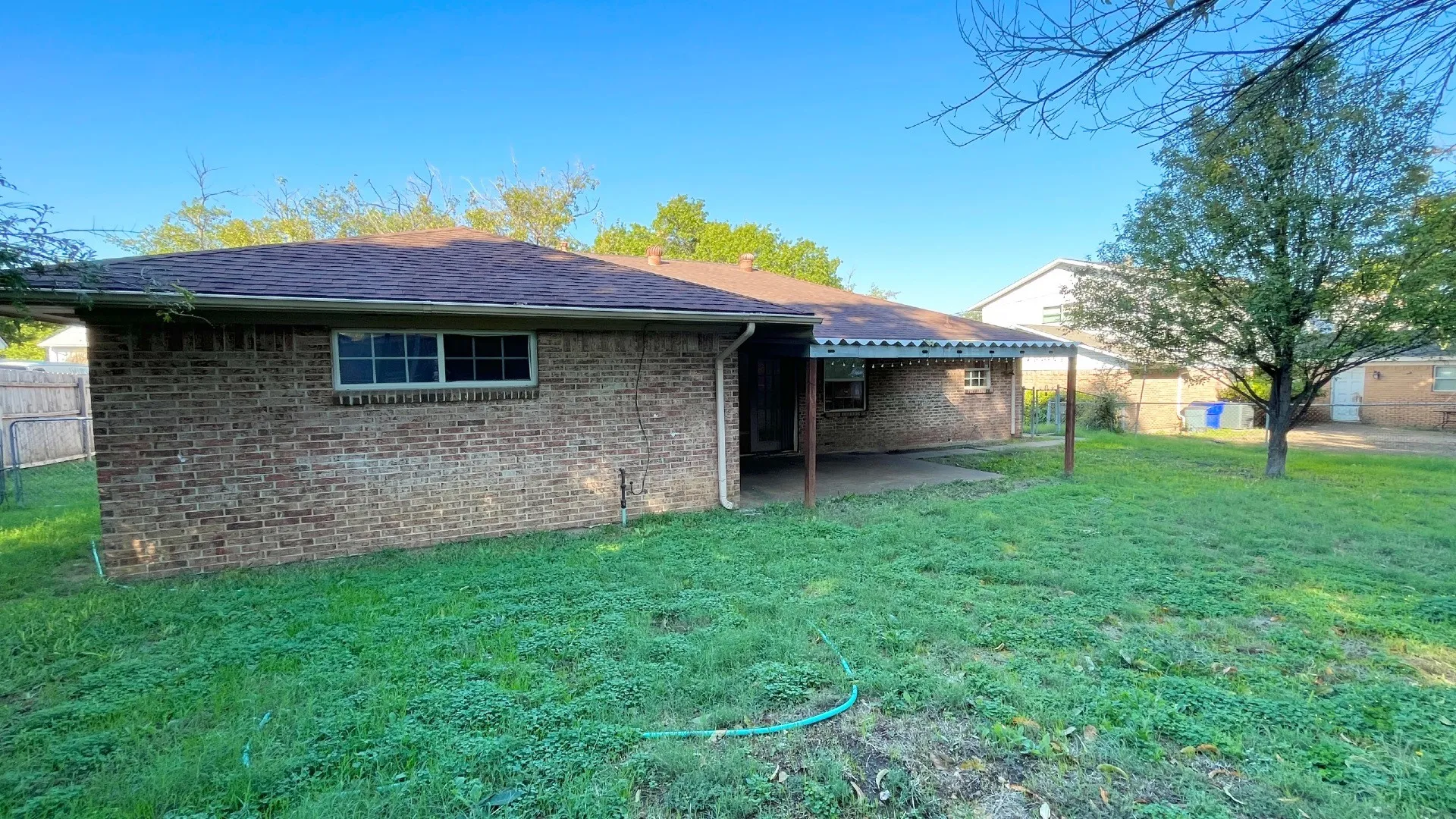 Brick exterior with a covered patio, a fenced perimeter, and a pitched shingle roof