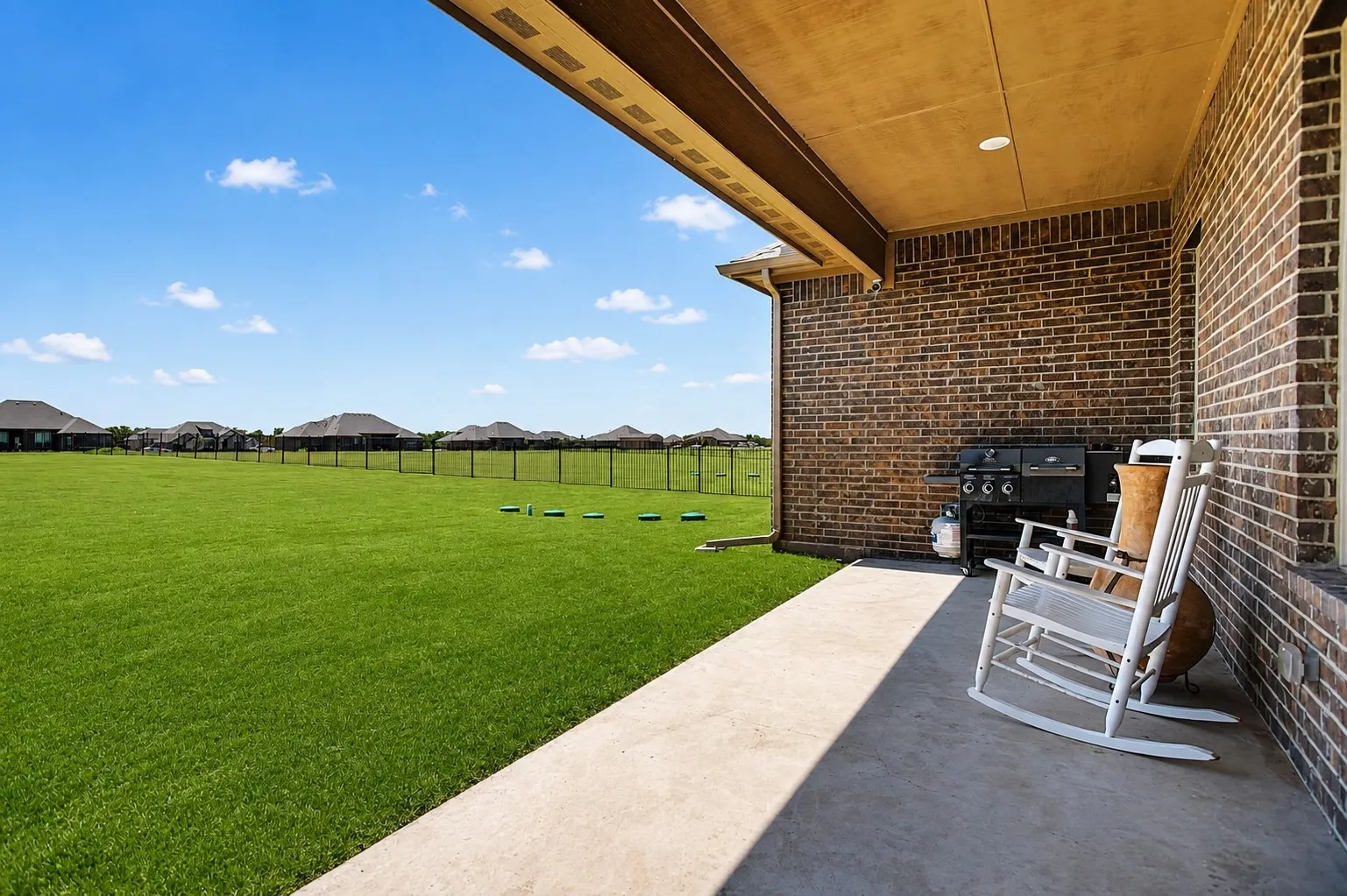 Expansive covered patio with recessed lighting, brick exterior, concrete flooring, and a large fenced yard with manicured lawn