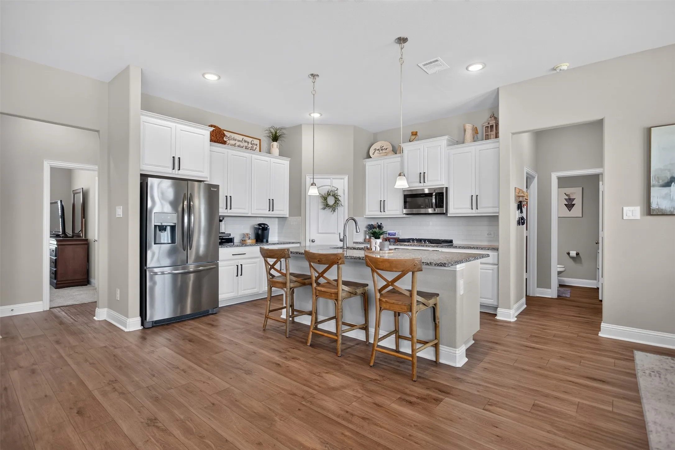 Open-concept kitchen featuring wood-finish flooring, white cabinetry with dark hardware, granite countertops, and stainless steel appliances