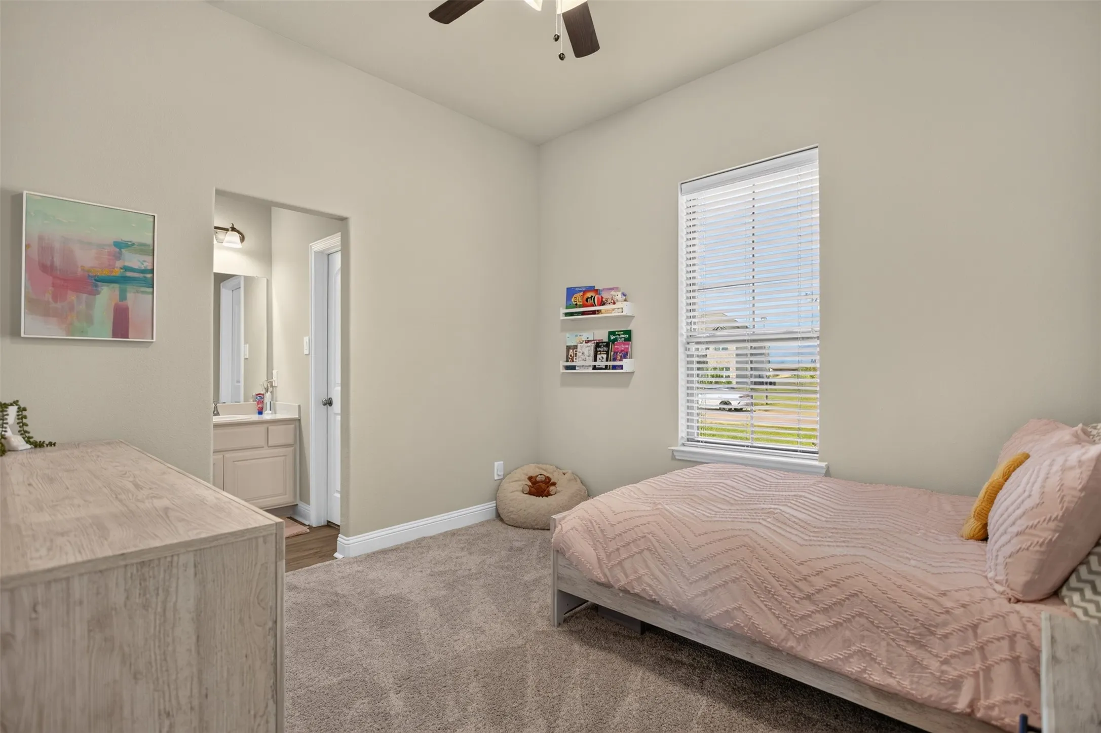 Soft grey wall paint, plush carpet flooring, recessed window, ceiling fan, and an attached vanity with a mirror