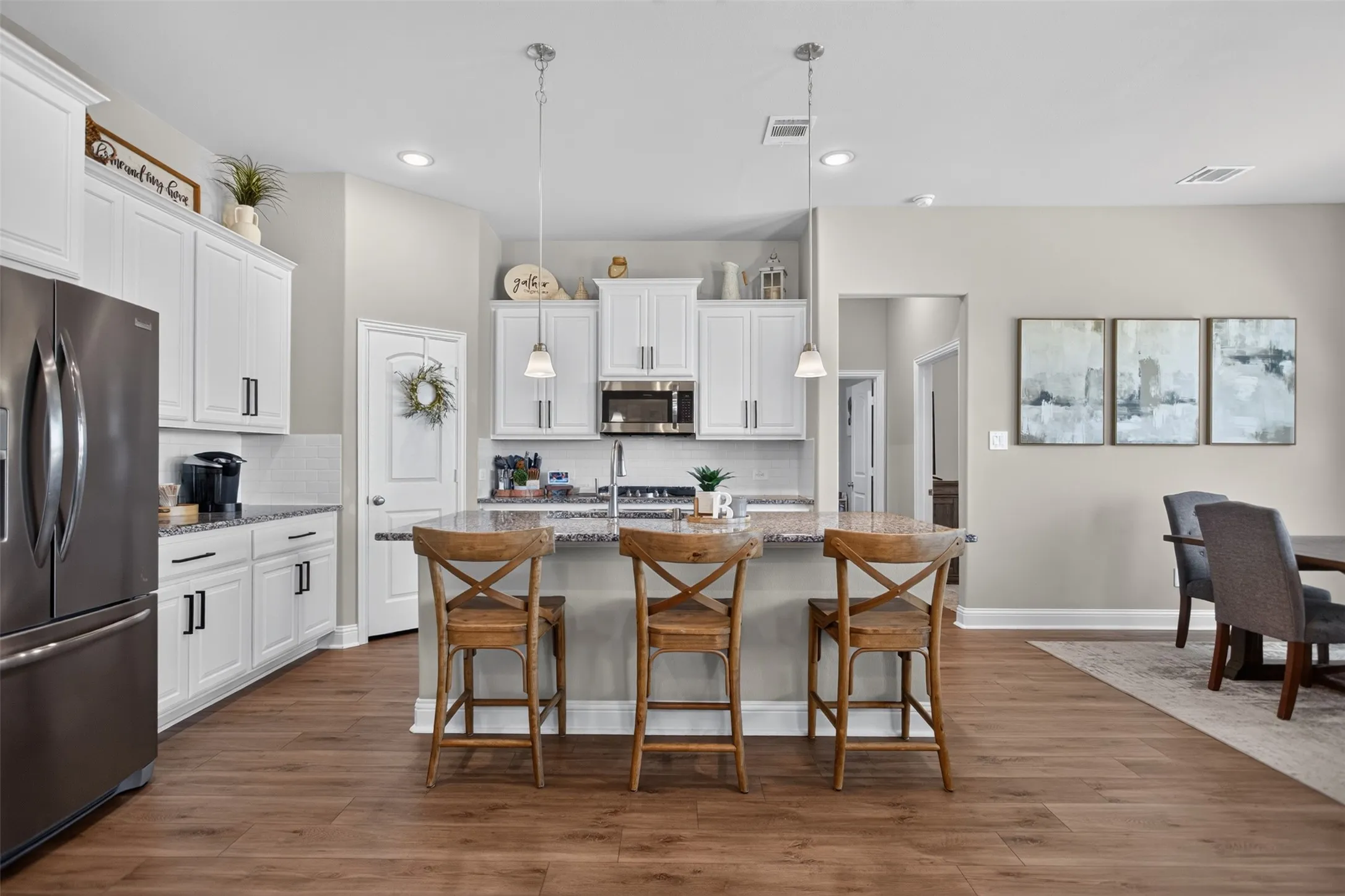 Kitchen featuring white cabinetry, stainless steel appliances, a center island with pendant lighting, and wood-finish flooring