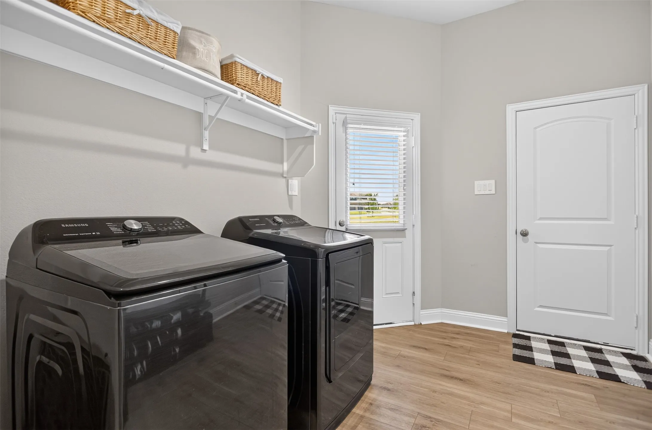 Laundry area with wood-finish flooring, overhead shelving, and a paneled door
