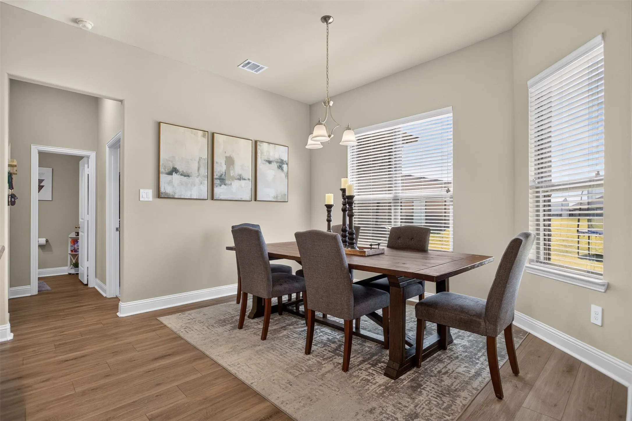 Wood-finish flooring throughout, complemented by a contemporary chandelier and natural light from multiple windows