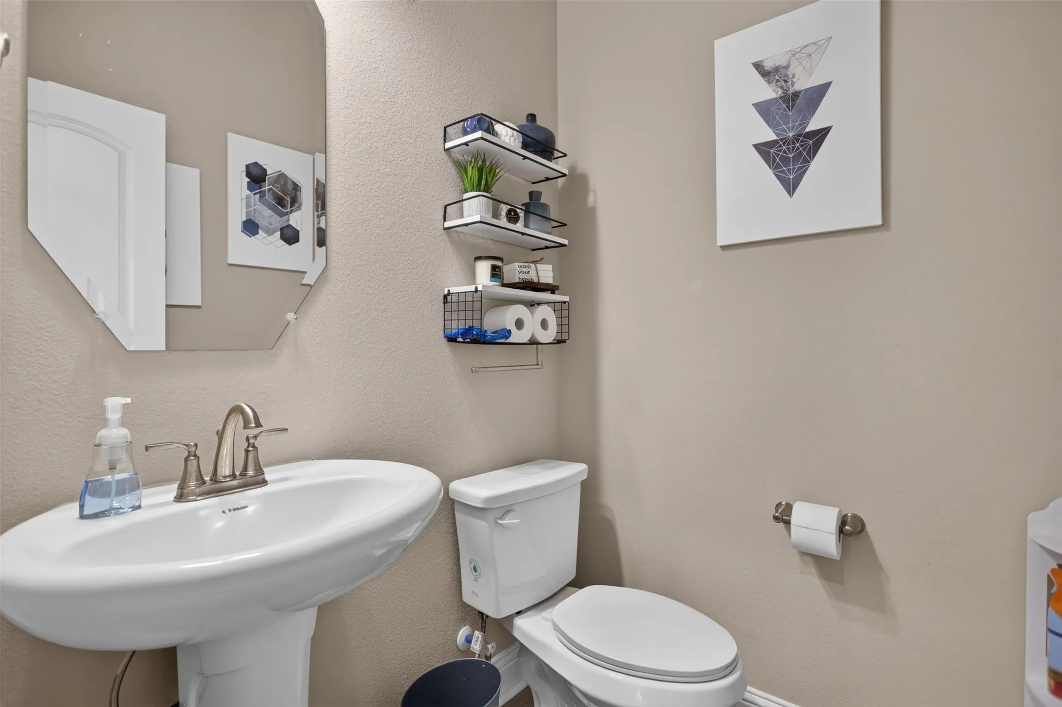 Pedestal sink with a brushed nickel faucet, an octagonal wall-mounted mirror, and wall-mounted storage shelving