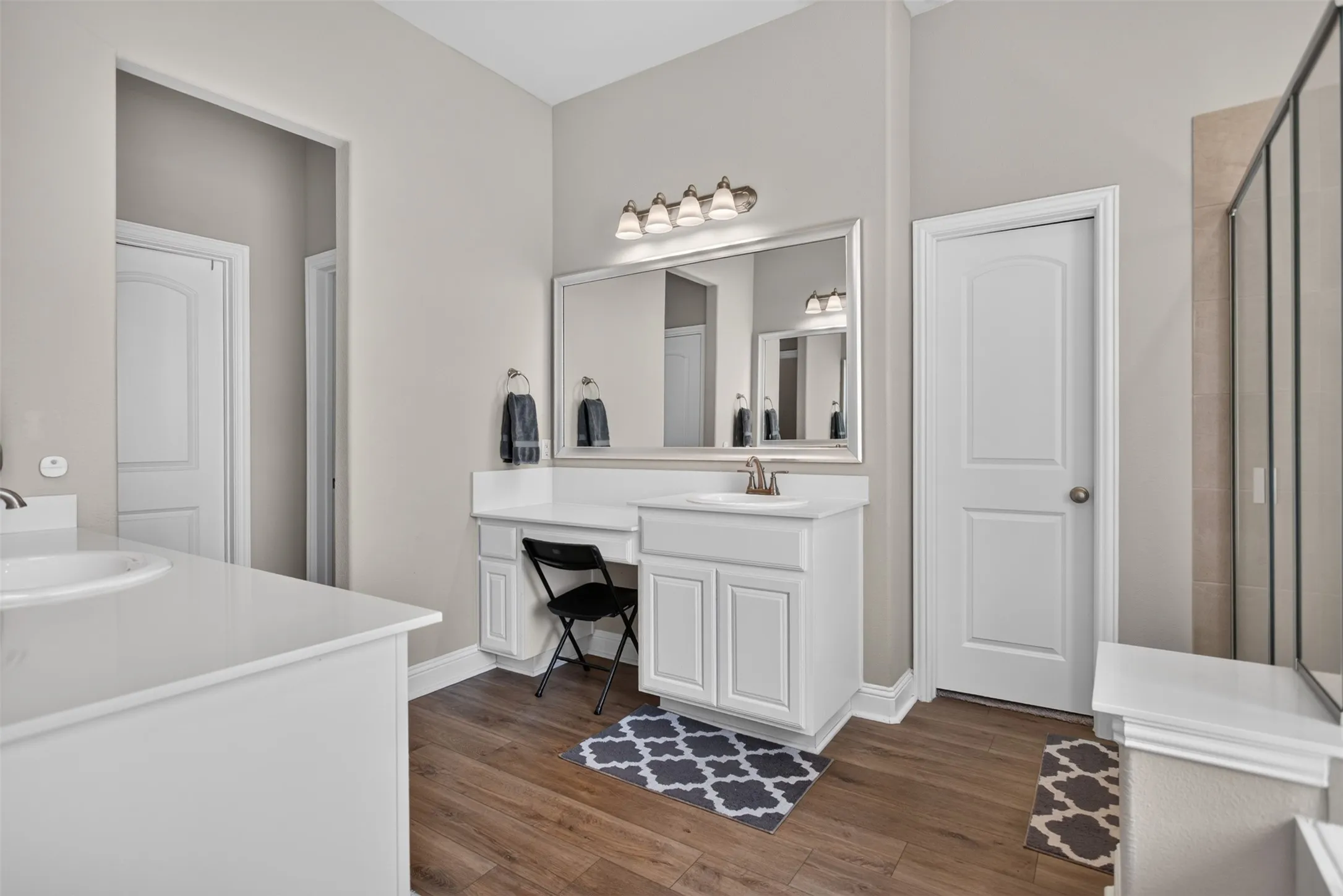 Dual vanity with white cabinetry, wood-finish flooring, a separate vanity area, and a glass-enclosed shower
