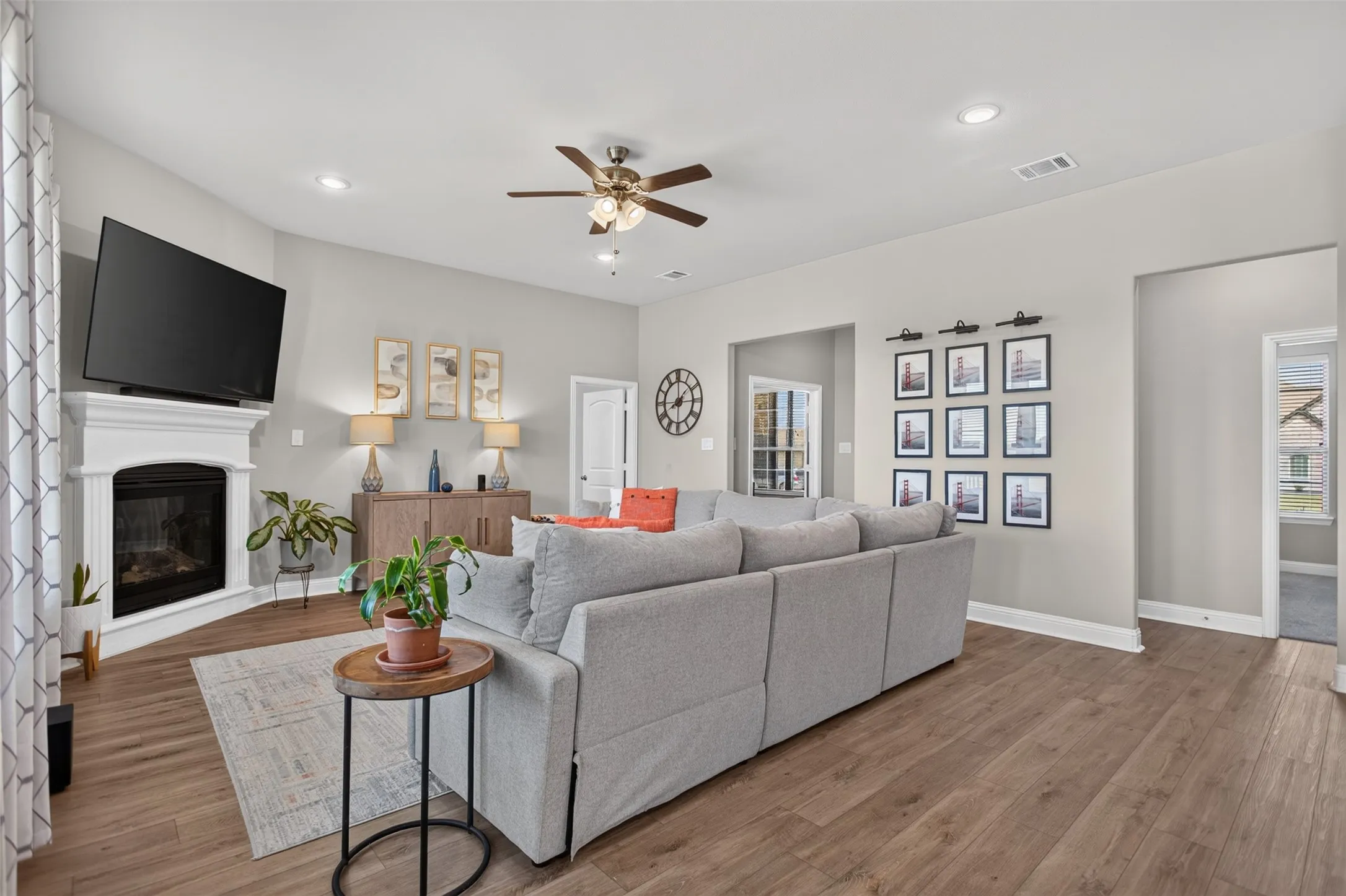 Wood-finish flooring, corner fireplace with white mantel, recessed lighting, ceiling fan, and light gray wall color