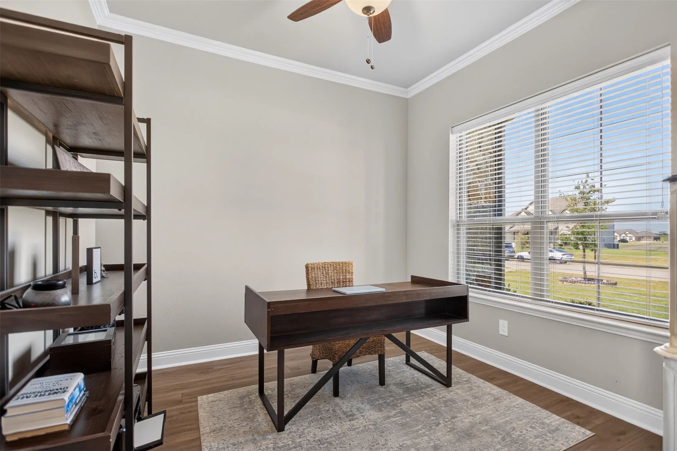 Crisp white trim, crown molding, a ceiling fan fixture, wood-finish flooring, and a large window with horizontal blinds