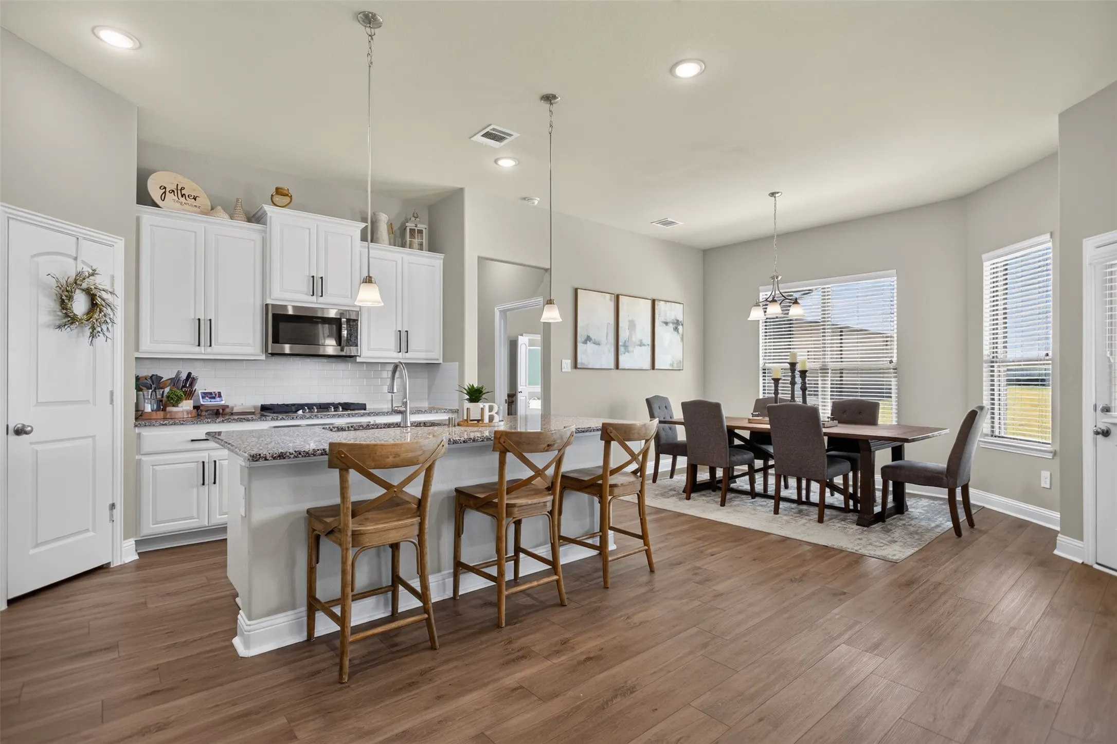 Open-concept living area with wood-finish flooring, white cabinetry, granite countertops, and stainless steel appliances
