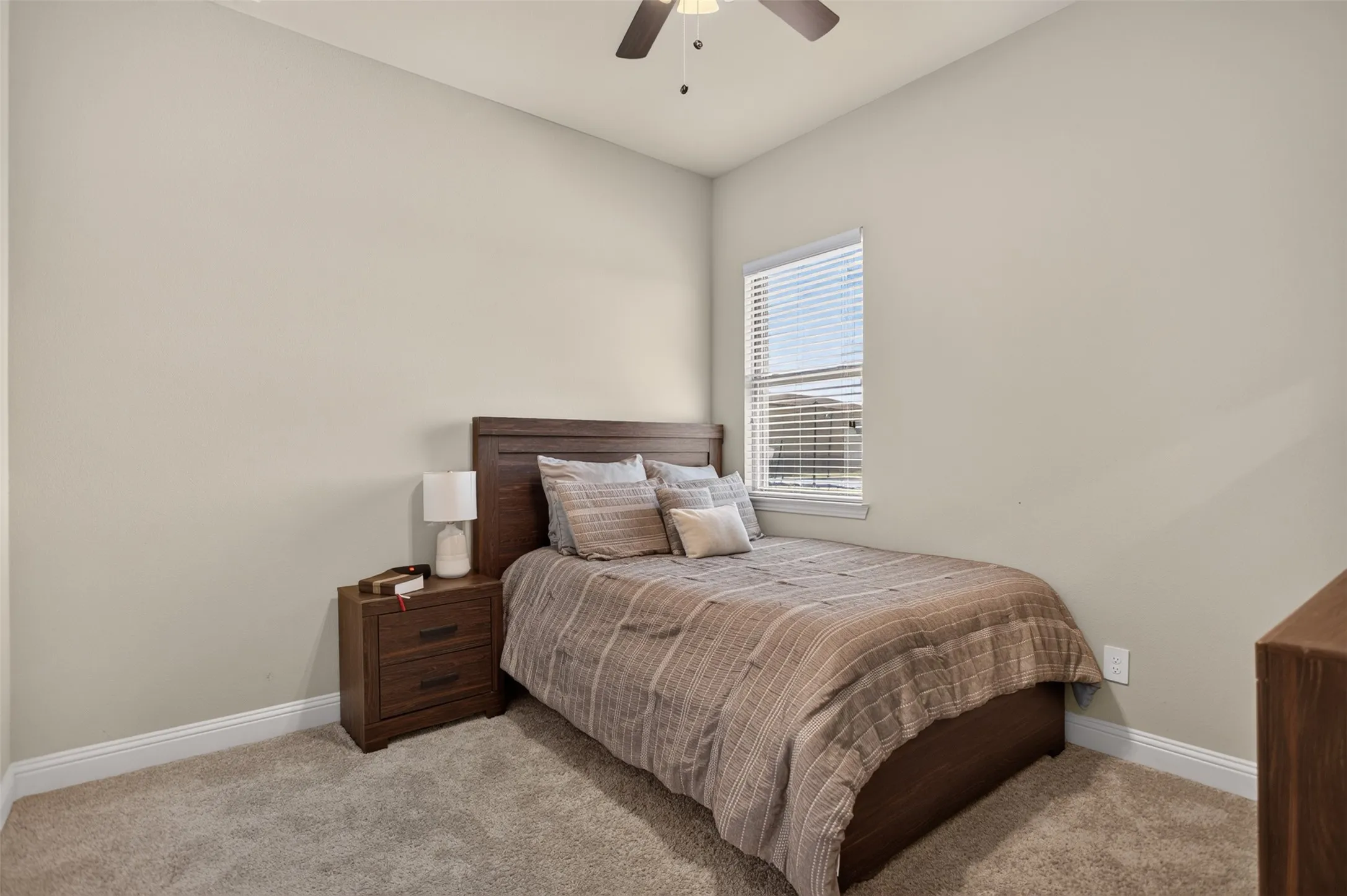 Neutral wall paint, carpet flooring, a window with blinds, and a ceiling fan with integrated lighting