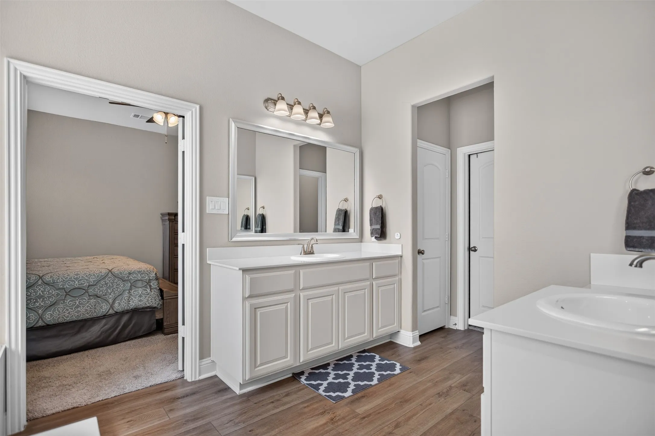 Double vanity with undermount sinks, wood-finish flooring, and a large wall-mounted mirror