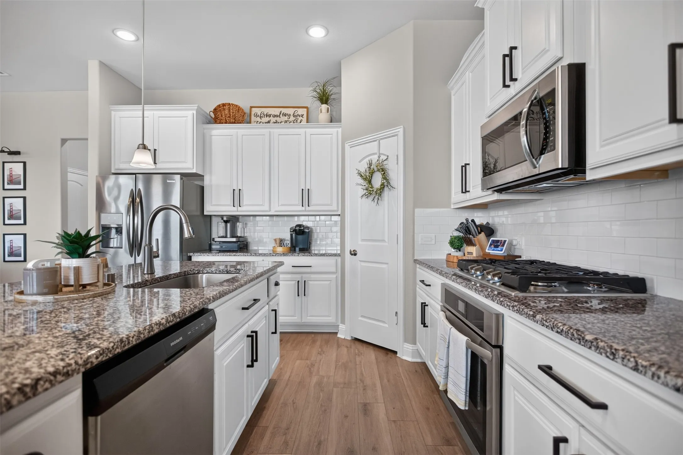 Kitchen featuring white cabinetry, stainless steel appliances, speckled stone countertops, a subway tile backsplash, and wood-finish flooring