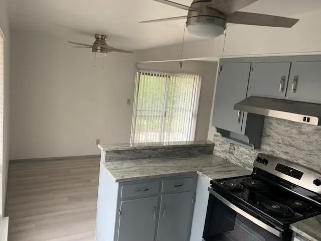 Kitchen and dining area featuring wood-finish flooring, ceiling fans, light gray cabinetry, and a range with a stainless steel vent hood