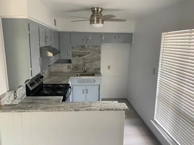 Kitchen featuring light gray cabinetry, stainless steel range hood, stone-finish countertops, and an integrated ceiling fan with lighting