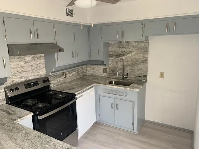 Kitchen featuring light gray cabinetry with brushed nickel hardware, expansive stone countertops, full-height stone backsplash, a stainless steel range, and wood-finish flooring