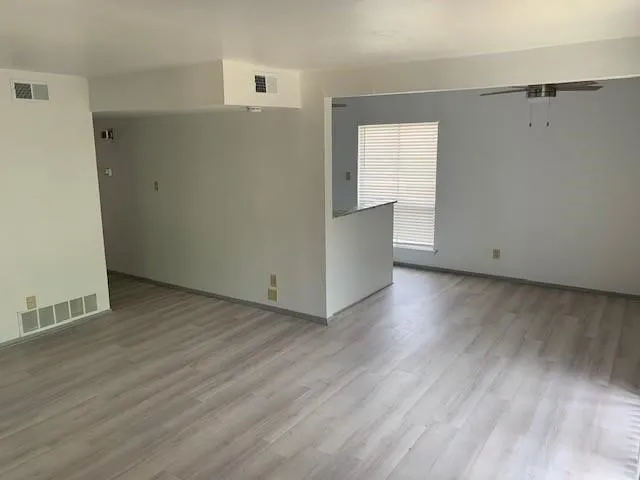 Wood-finish flooring throughout, neutral paint palette, window with horizontal blinds, ceiling fan, and a half-wall with a counter surface