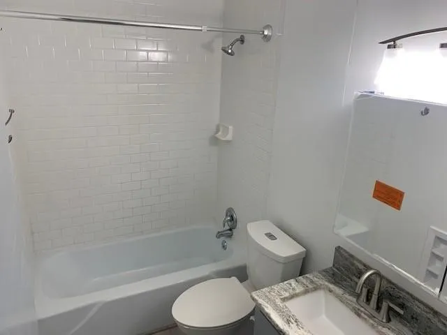 White subway tile shower surround, chrome shower fixtures, white porcelain tub, gray stone-finish vanity countertop, and chrome faucet