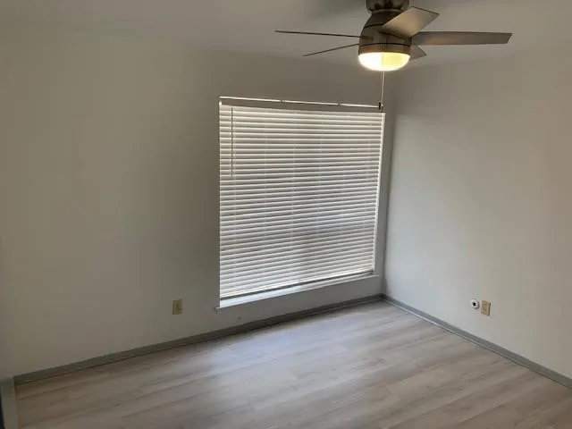 Window with blinds, overhead ceiling fan with integrated lighting, and wood-finish flooring