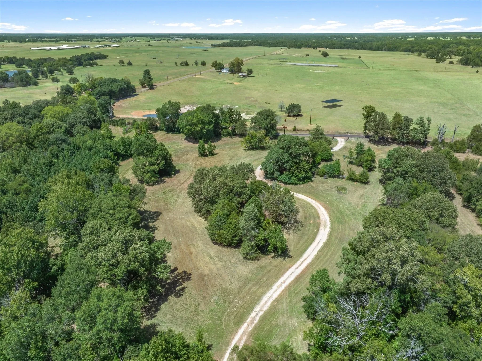 Expansive grounds featuring a winding drive, mature trees, open fields, and distant structures