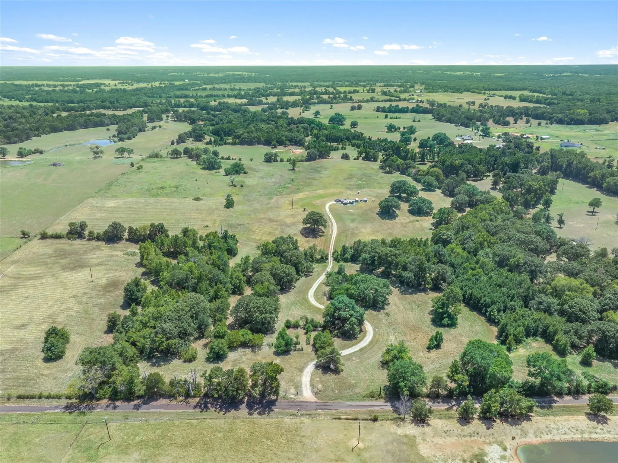 Expansive rural landscape featuring scattered trees, open fields, and a winding driveway