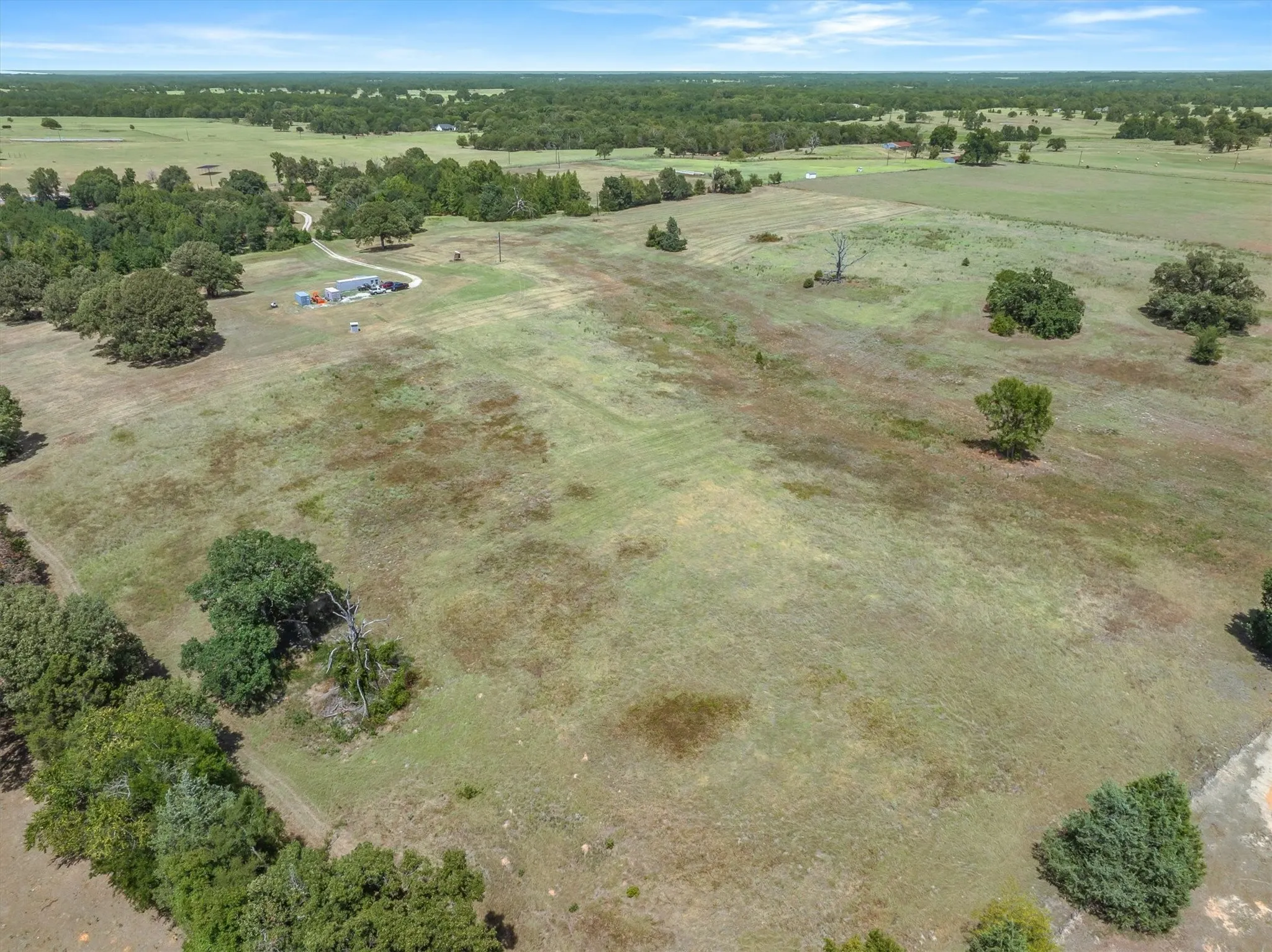 Expansive land parcel featuring a winding gravel drive, scattered mature trees, and a distant building