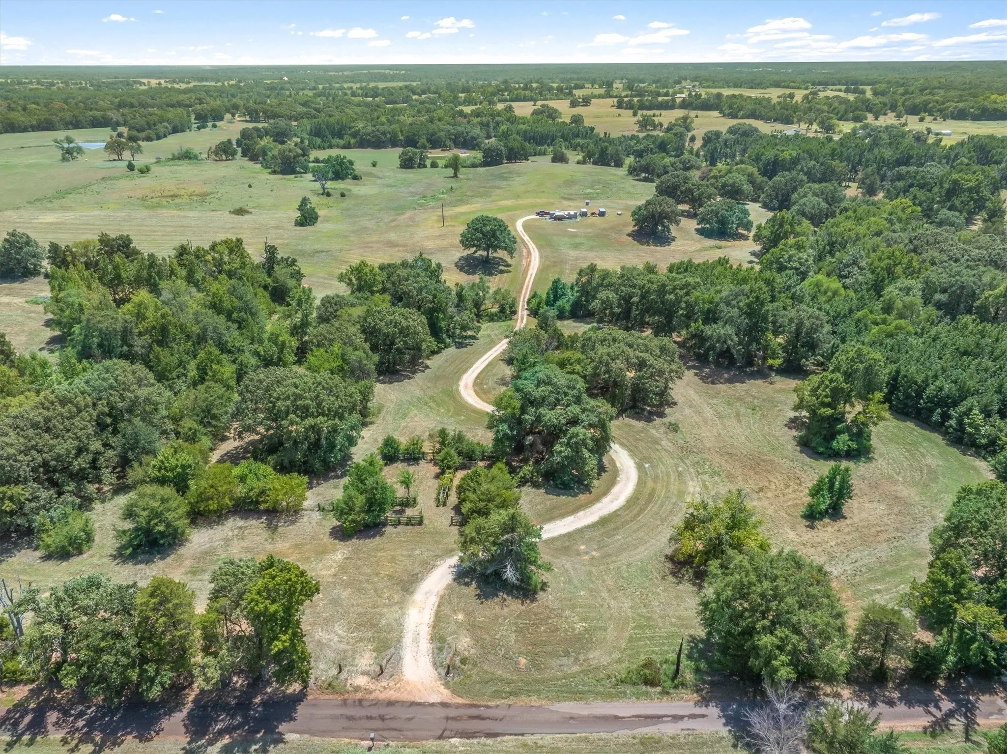 Expansive green acreage featuring a winding gravel drive, mature trees, and open fields
