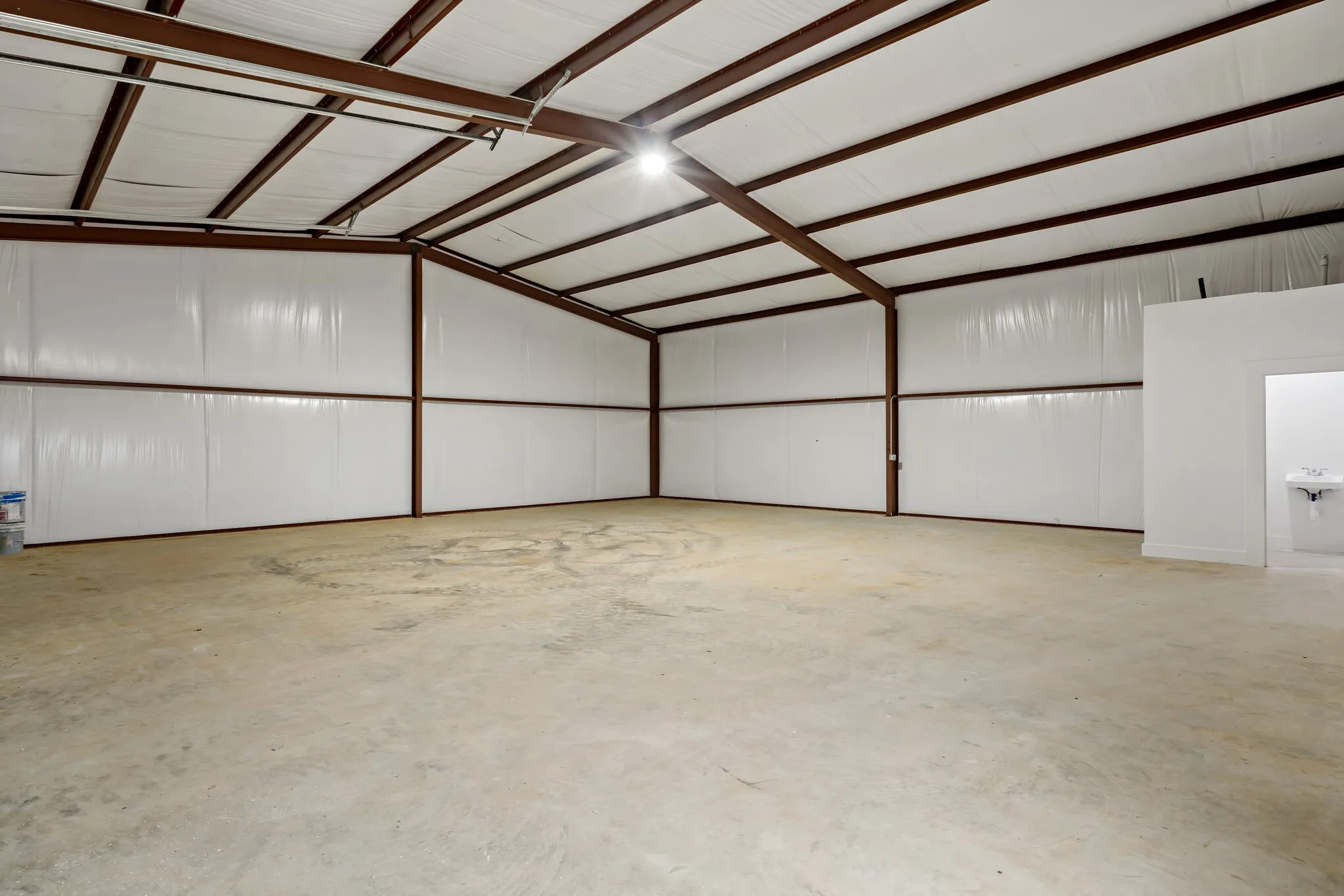 Spacious concrete-floored interior featuring exposed metal beam construction and white insulated paneling