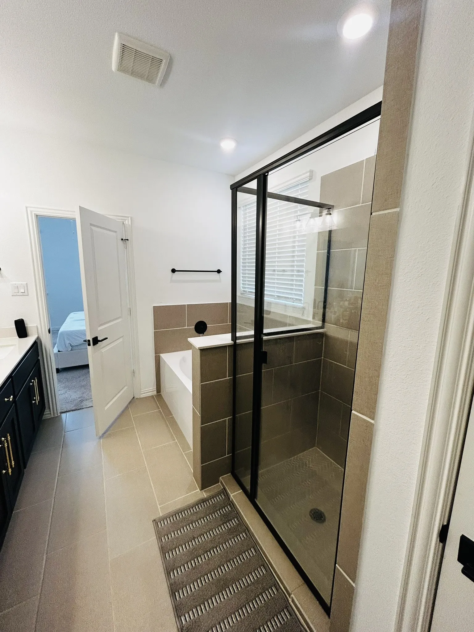 Tile flooring, built-in bathtub, glass-enclosed shower, wall-mounted light fixture, recessed ceiling lights