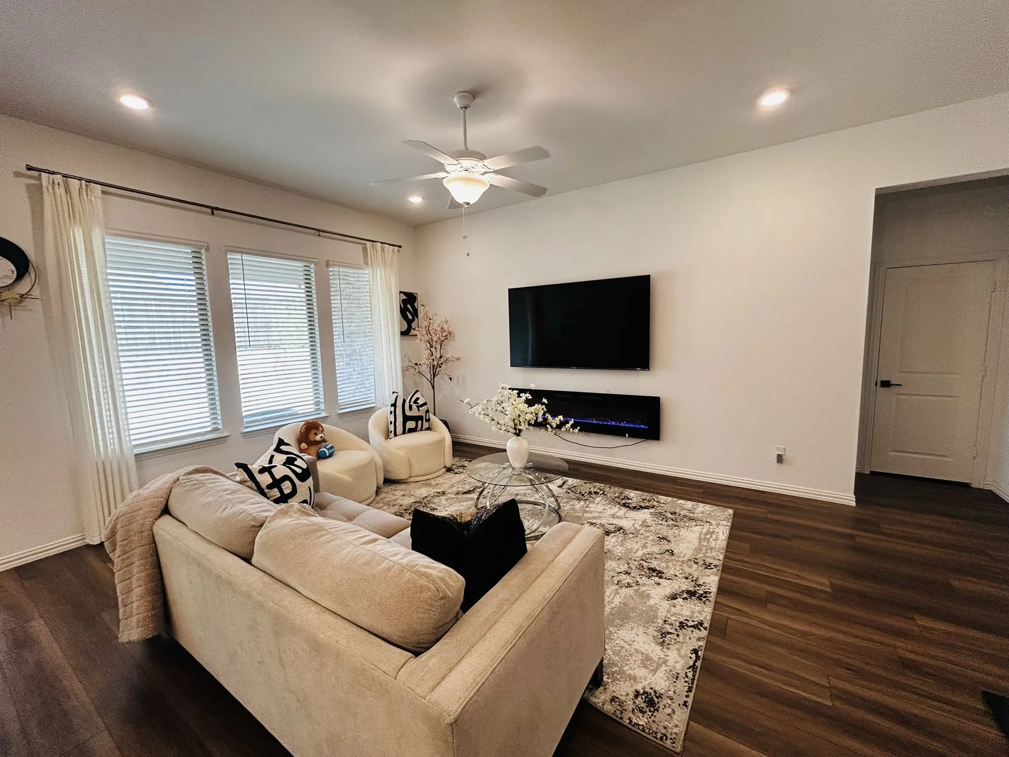 Wood-finish flooring, recessed lighting, ceiling fan, multiple windows with blinds, and a built-in wall fireplace