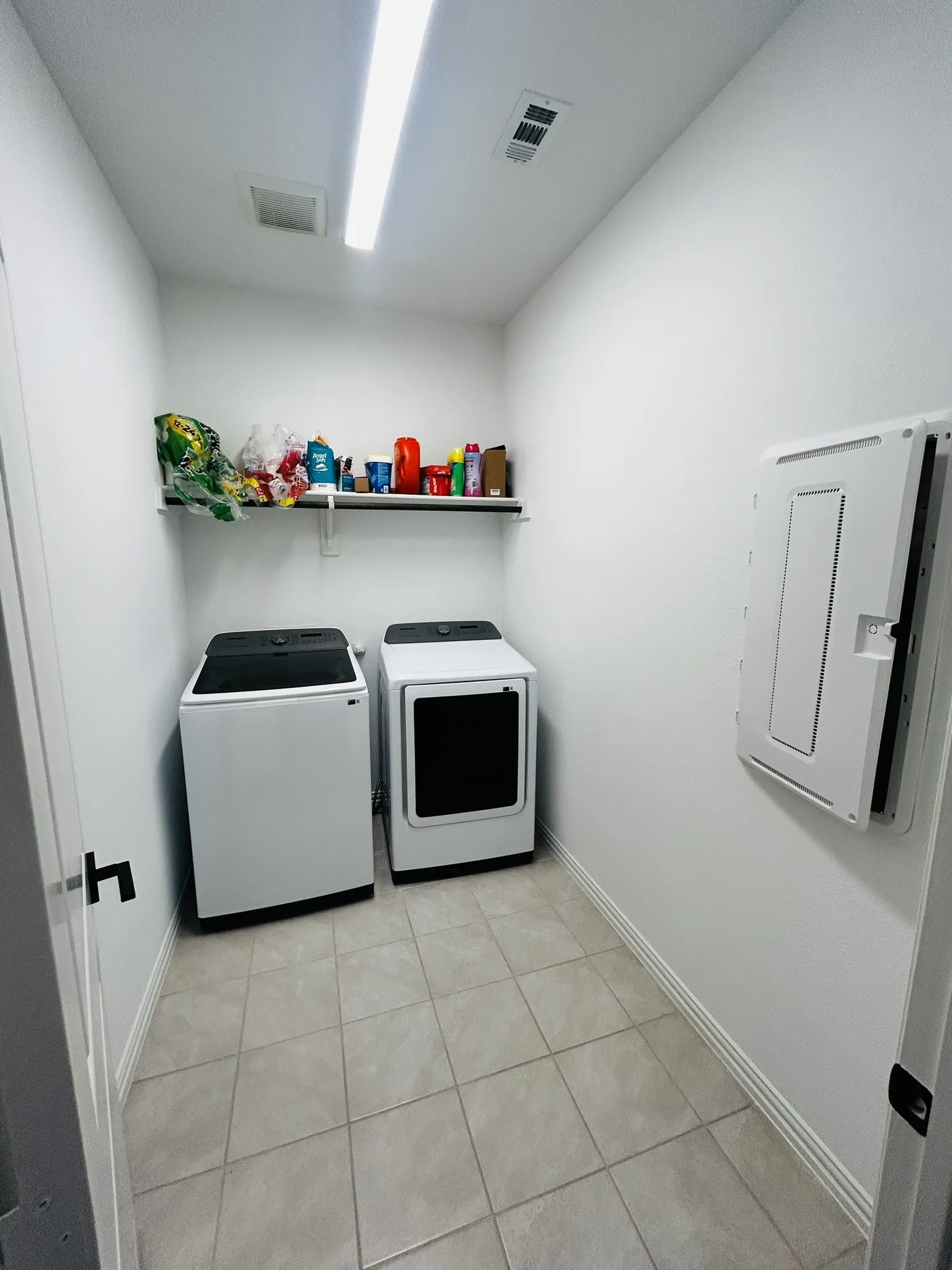Laundry area featuring tiled flooring, a wall-mounted shelf, and overhead strip lighting