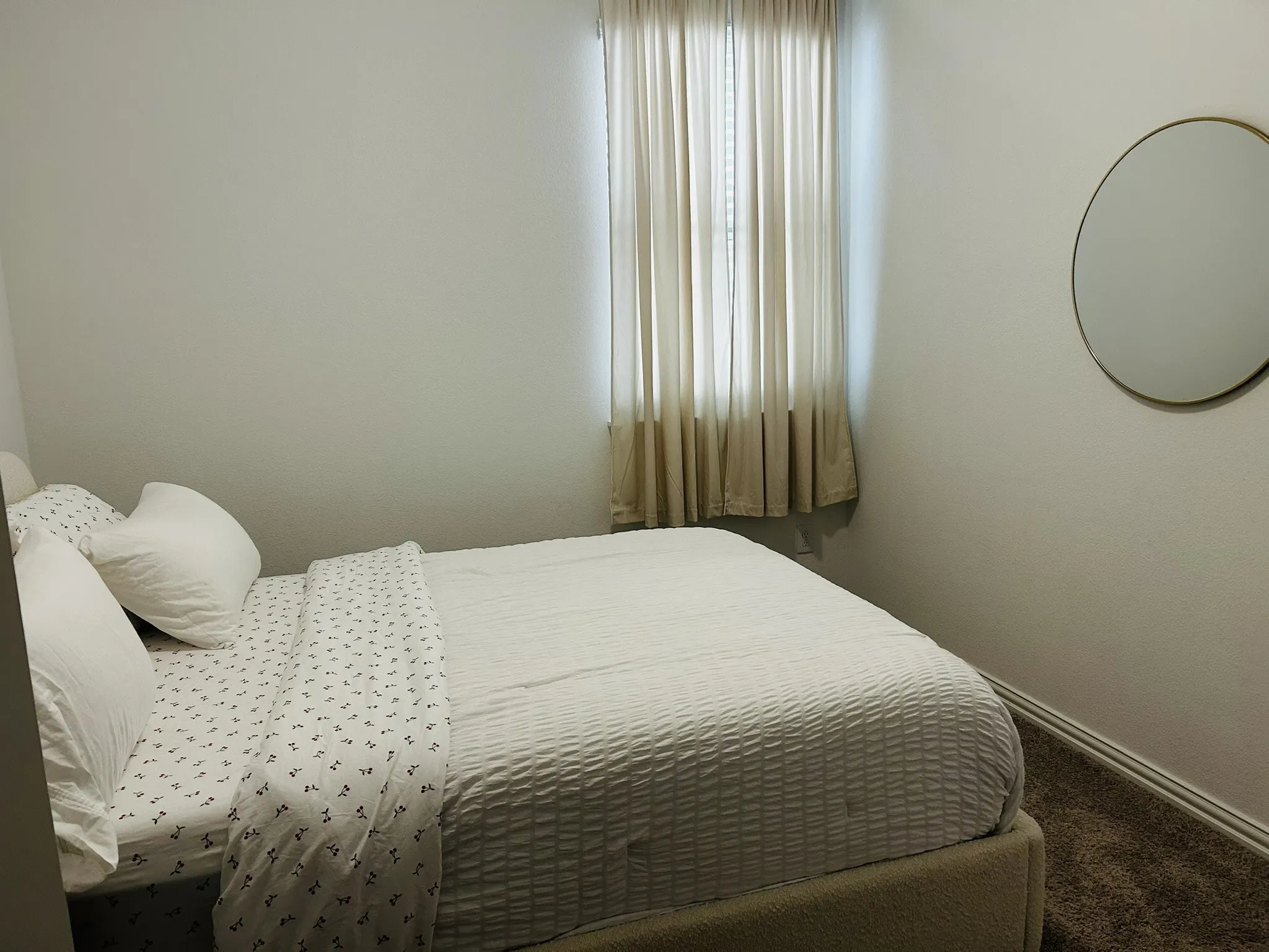 Textured wall finish, window with full-length drapes, wall-mounted circular mirror, and carpeted flooring