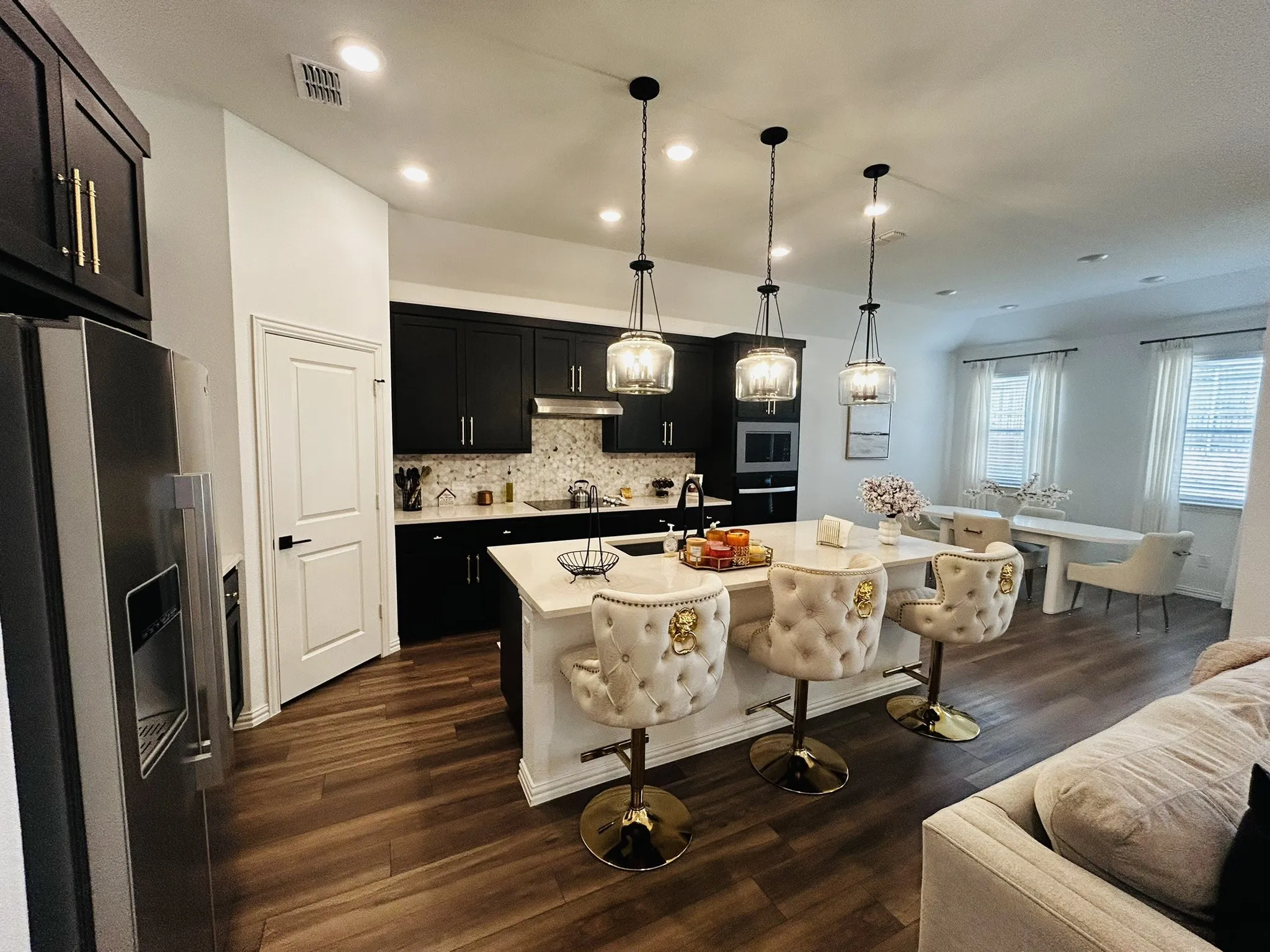Contemporary kitchen featuring dark cabinetry, stainless steel appliances, a center island with pendant lighting, and wood-finish flooring